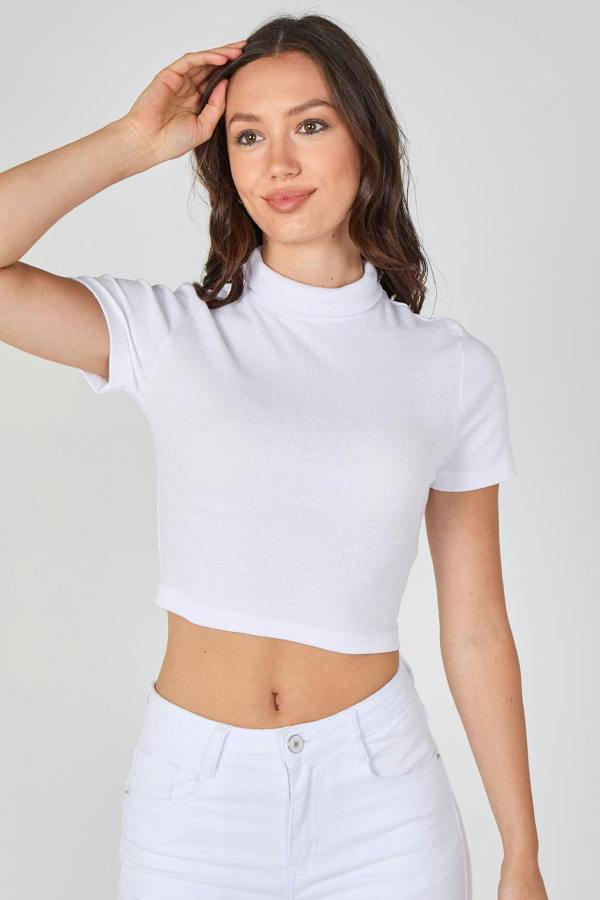 Woman wearing a white crop top and white pants against a plain background