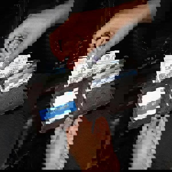 Person holding a brown leather wallet with cards and money in a car interior.