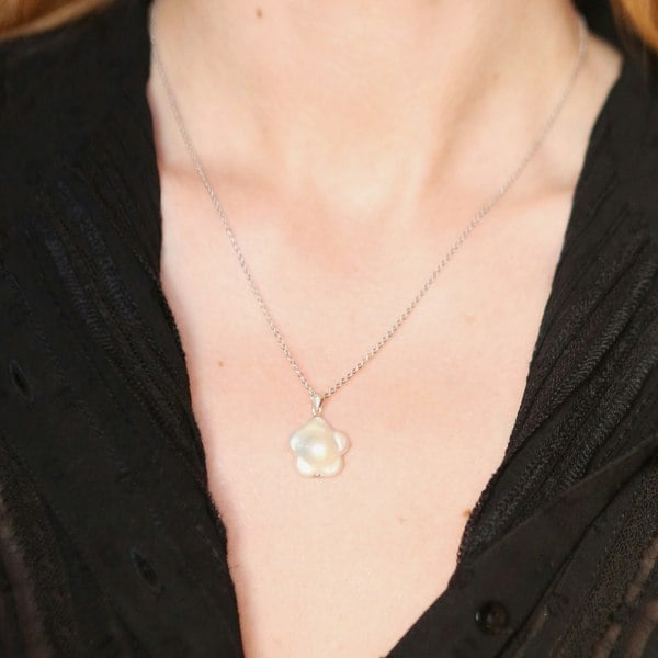 Flower-shaped pearl pendant in rhodium-plated silver by LENAE worn by a model.