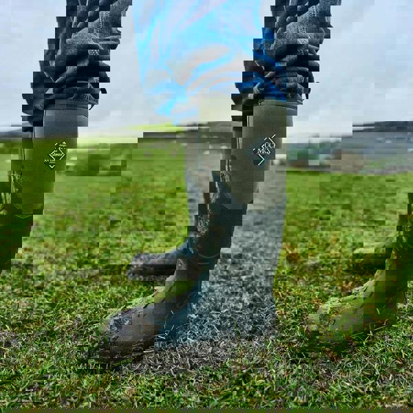 Muck Boots MUCK Boots Chore 2k Mens Classic Stable Farm Tall Wellington Wellies, image of a person wearing green and black insulated waterproof rubber boots standing on a muddy field.