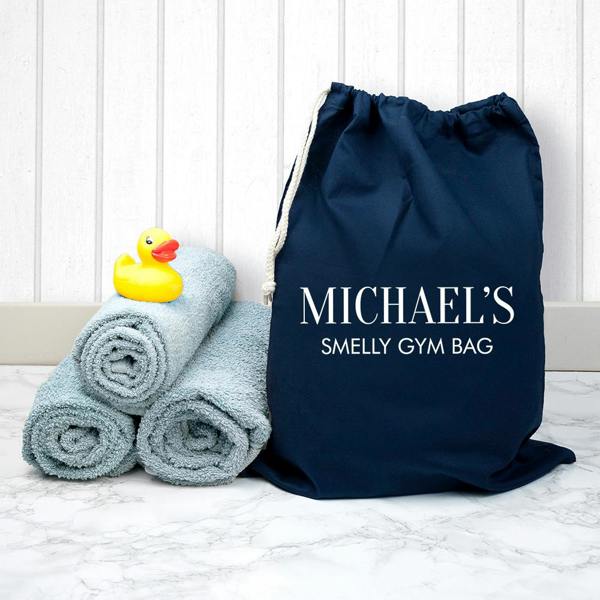 A dark navy personalised cotton drawstring bag printed with Michael's Smelly Gym Bag in white uppercase letters, sitting next to a stack of blue towels and a yellow rubber duck.
