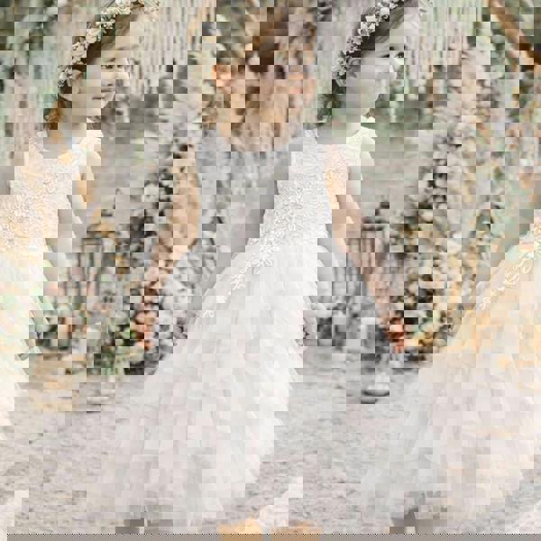 Young girl in a white floral dress standing in a decorated outdoor setting with flowers and lanterns.