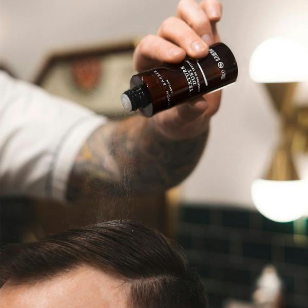 Barber holding a bottle of texture dust applying the powder to a male clients hair