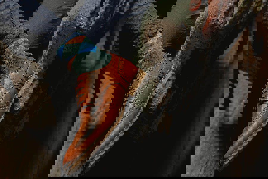 Brown leather shoe with a colorful sock worn by a person sitting on a stone bench.