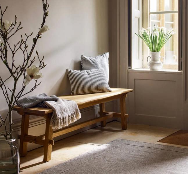 Reclaimed teak bench styled with cushions and a throw in a neutral hallway.