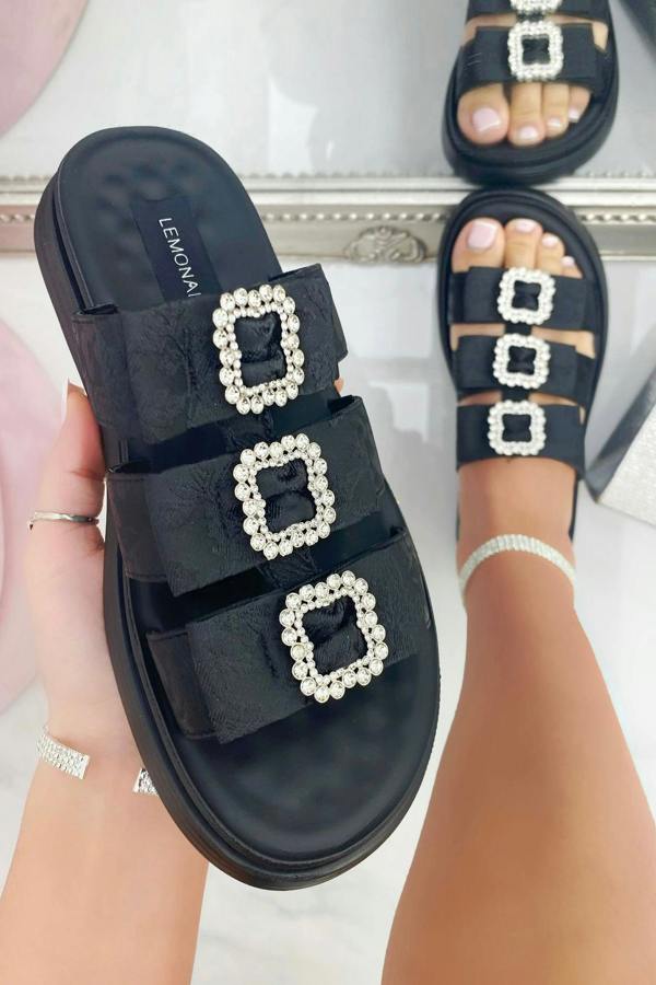 Black sandals with square pearl embellishments worn by a person on a light background