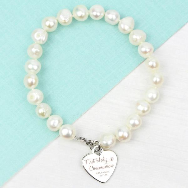 Personalised white freshwater pearl communion bracelet with an engraved rhodium-plated heart tag inside an open white presentation box.