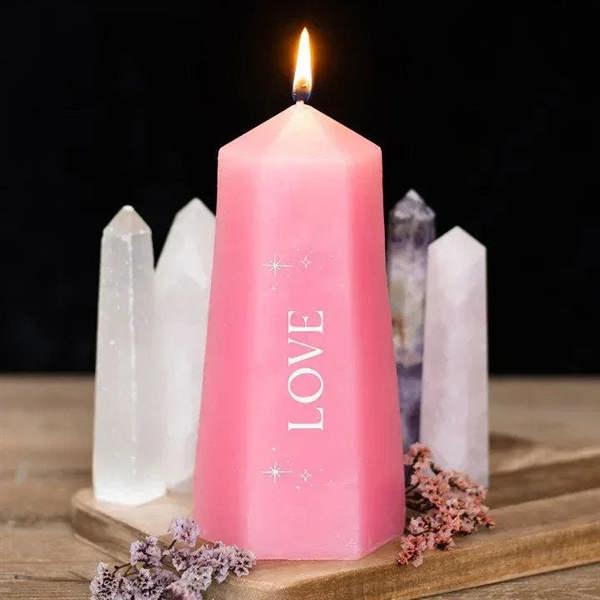 Pink faceted Love pillar candle with flame, beside rough rose quartz crystals