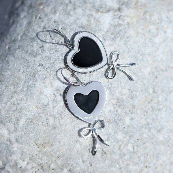 Silver heart earrings on a rocky surface.