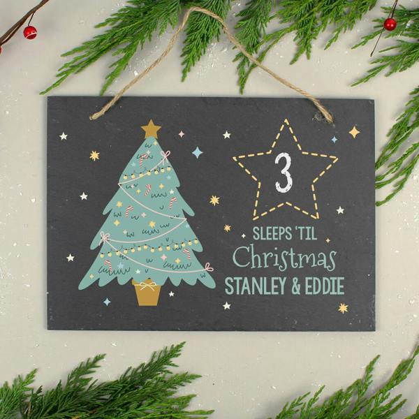 A personalised Christmas countdown slate sign printed with the number 3 and the names STANLEY & EDDIE, hanging against a grey background with pine branches.