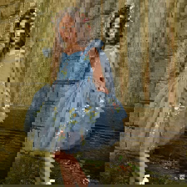 Young girl in a blue floral dress standing against a rustic stone wall.