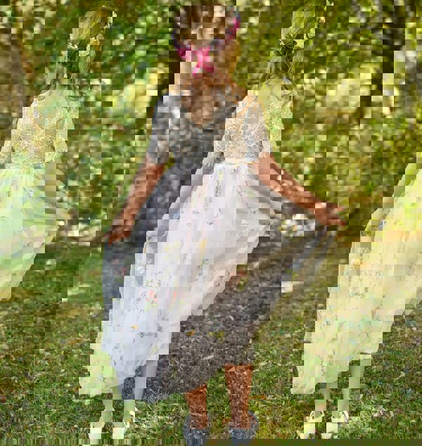 Young girl in a floral dress standing outdoors with greenery in the background