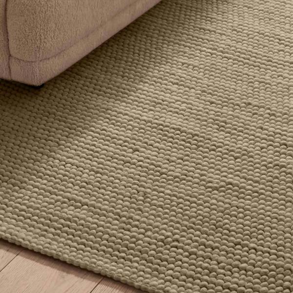 Close-up of a textured beige rug on a wooden floor.