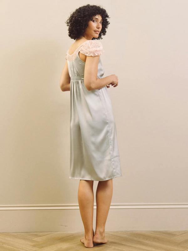 Woman wearing a light blue slip nightdress with lace trim against a beige wall.
