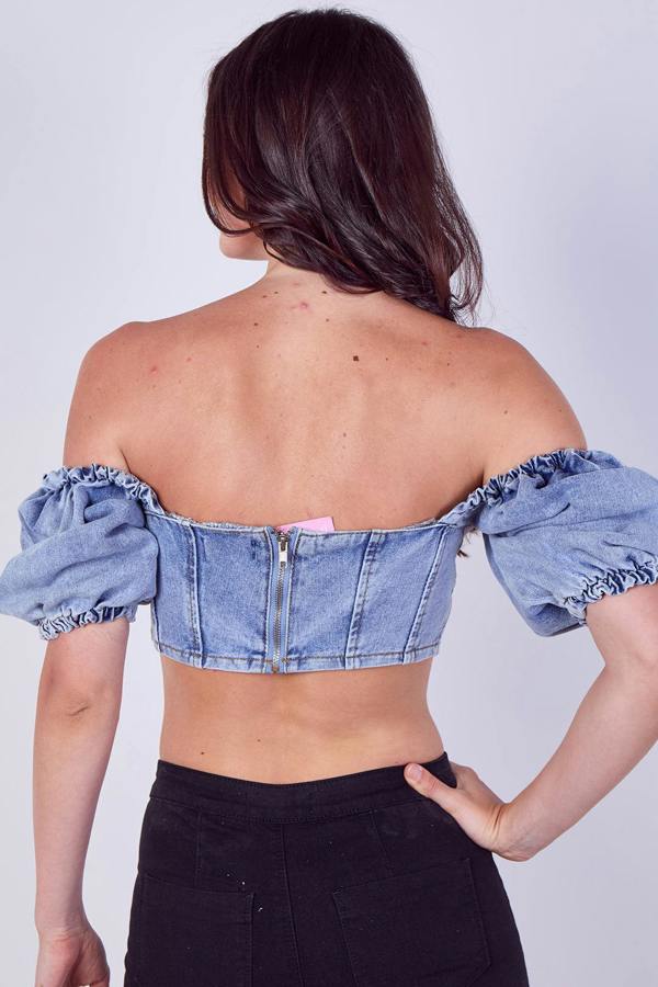 Person wearing a denim off-shoulder top against a plain background
