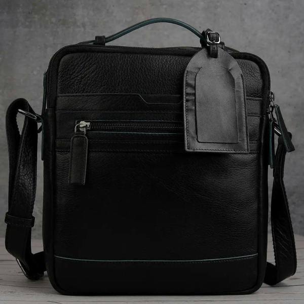 Black leather luggage tag attached to matching leather shoulder bag for coordinated travel style.