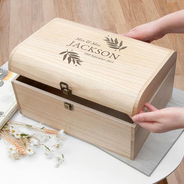 A large Paulownia wood keepsake chest with a curved lid, engraved with "Mrs & Mrs Jackson" and a wedding date, being held by hands.