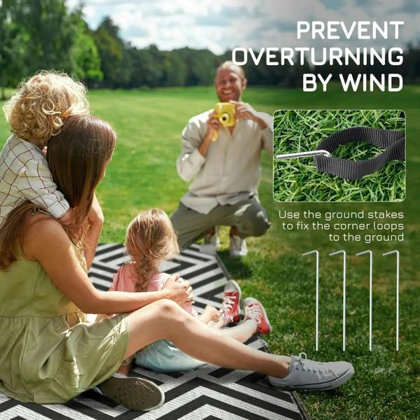 Black and white reversible outdoor rug secured with ground stakes on a patio