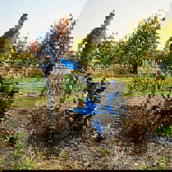 7.5hp petrol rotavator in action, featuring a blue body, sturdy wheels, and a powerful engine, tilling rich soil in a garden setting