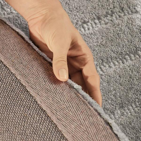 Hand touching the edge of two different textured carpets.
