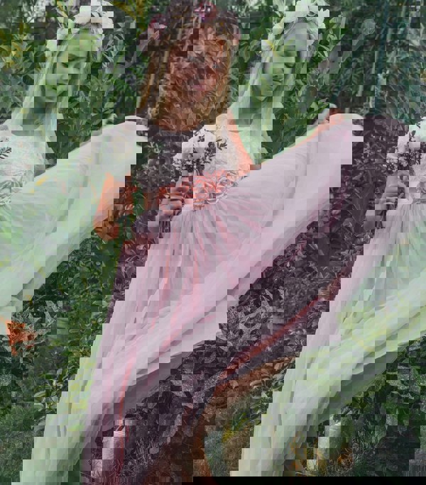 Young girl in a pink dress with floral headband and bouquet, standing in a garden.