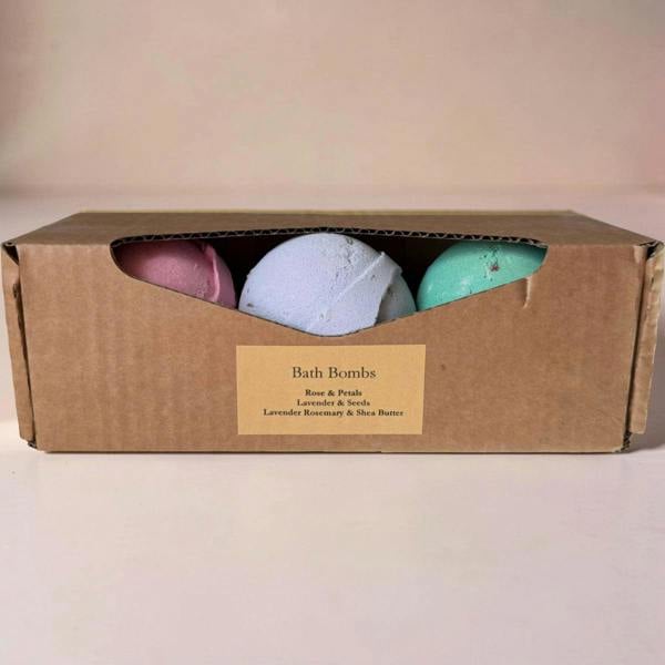 Three bath bombs in a cardboard box with a label on a beige background