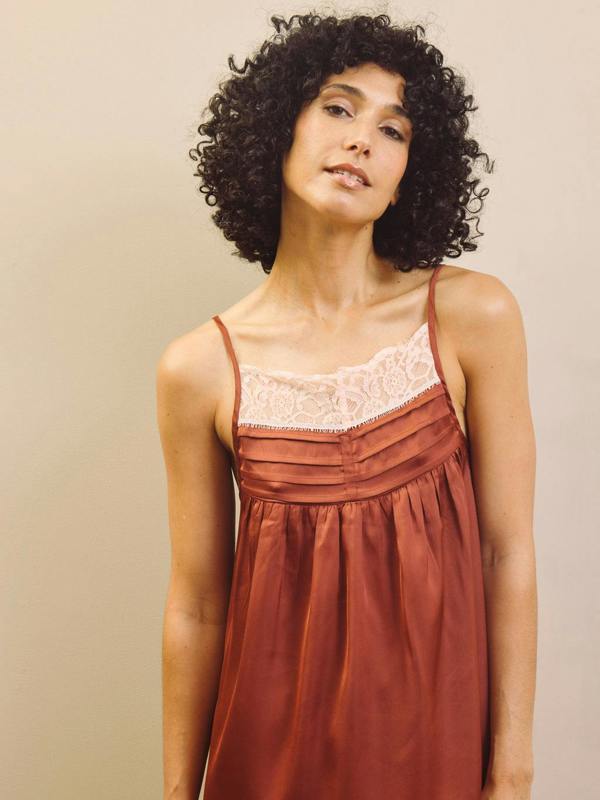Woman wearing a rust-coloured pyjama cami top with lace details against a beige background