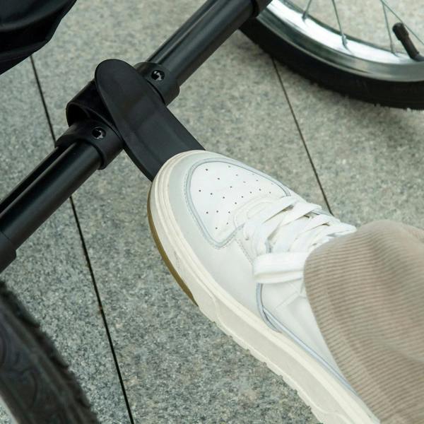 Black stroller handle with white sneaker stepping for jogging, close-up detail