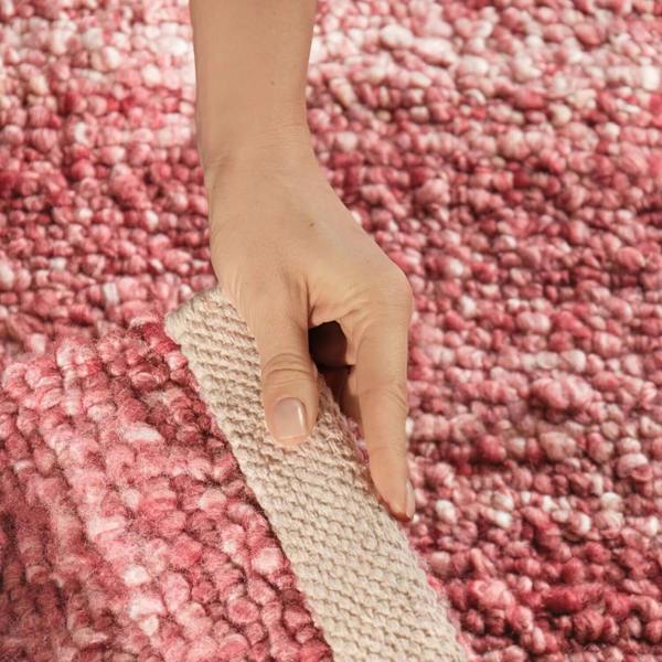 Hand holding a textured strip against a pink carpet