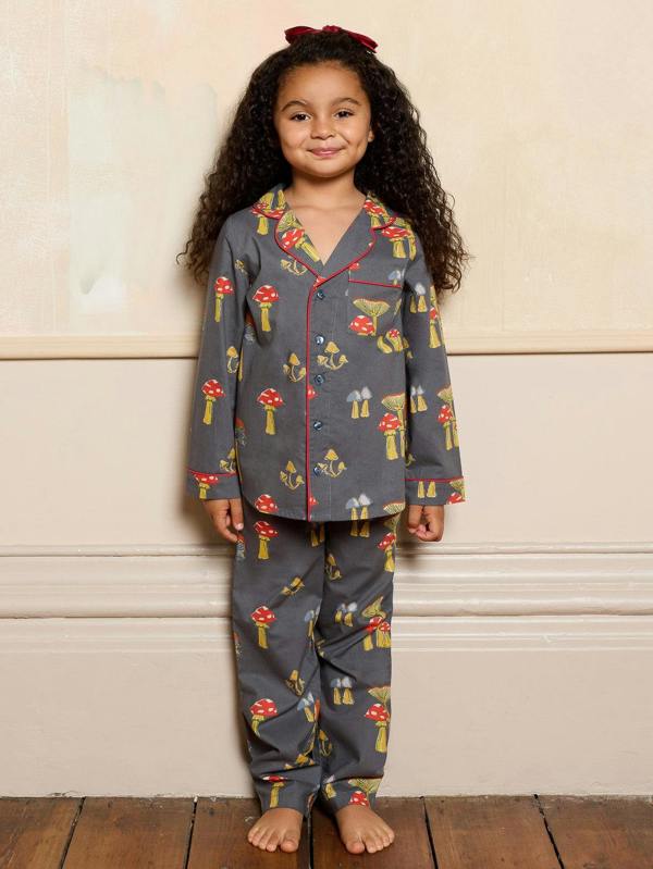 Child wearing a grey mushroom patterned pyjama set standing against a beige wall.