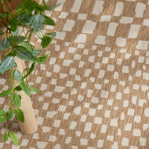Brown woven fabric with a geometric pattern and a plant in the foreground.