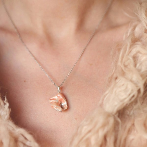 Close up of a model wearing shell pendant charm by LENAE London, featuring natural shells in coral colour.