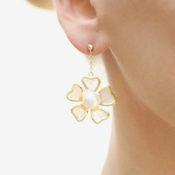 A close up of an ear with a baroque pearl and mother of pearl flower drop earrings.