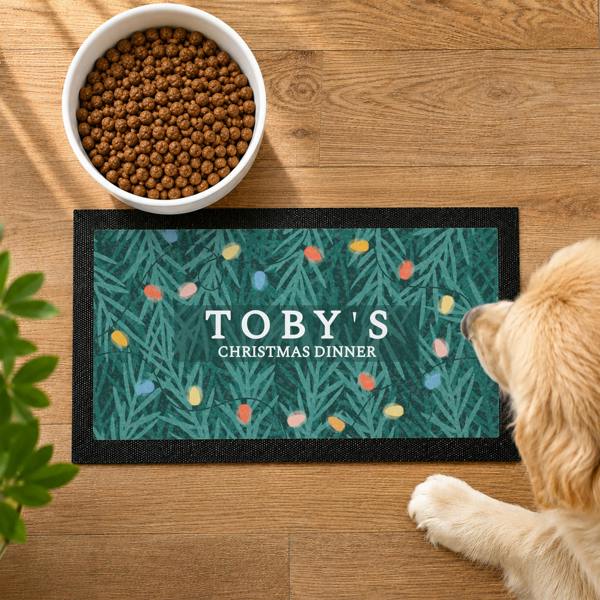 Overhead view of a personalised Christmas pet bowl mat with a retro fairy light pattern and text reading TOBY'S CHRISTMAS DINNER.