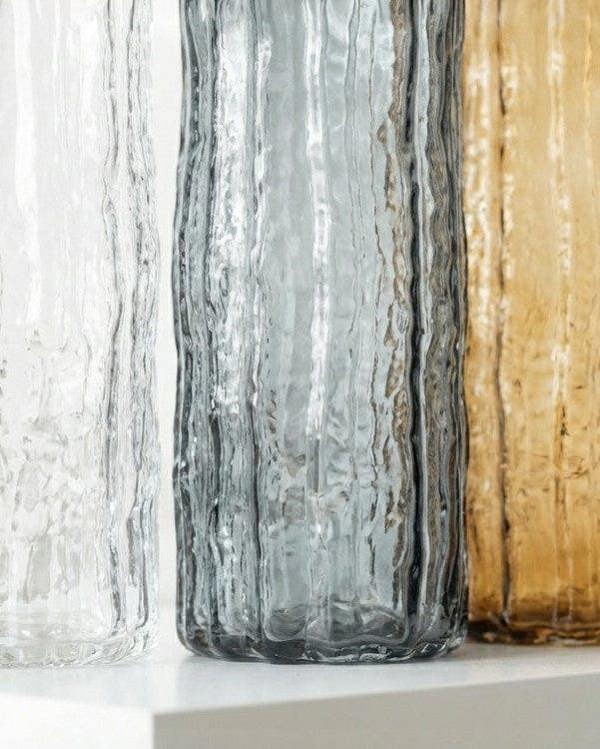 Three textured glass vases in clear, black, and gold on a wooden surface.