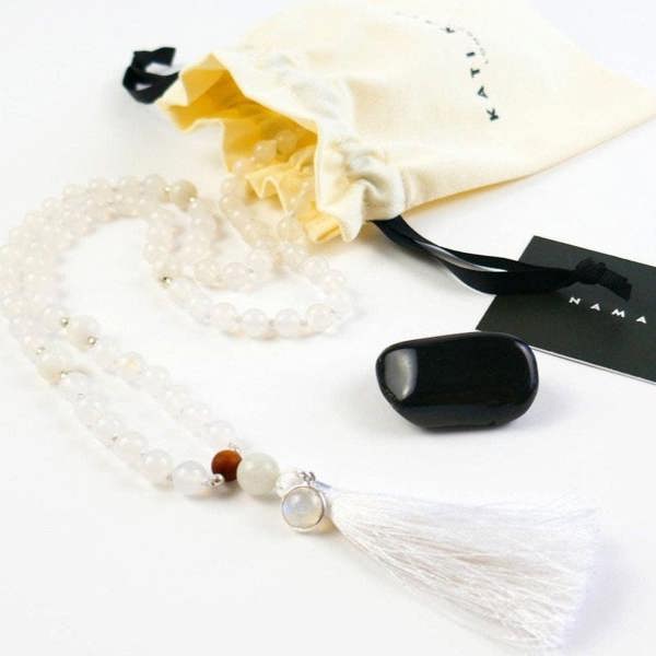 Kati Kaia crystal moonstone mala necklace with white beads and tassel next to cream pouch and black stone