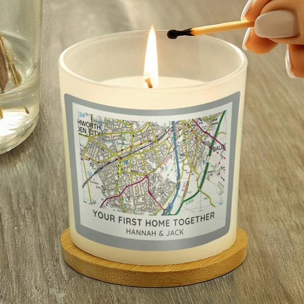 A hand lighting a personalised new home map candle with a match on a wooden coaster.
