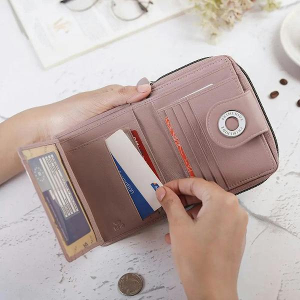 Person opening a pink wallet to reveal cards and coins on a light surface.