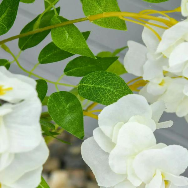 Close-up of white artificial wisteria flowers and textured green leaves