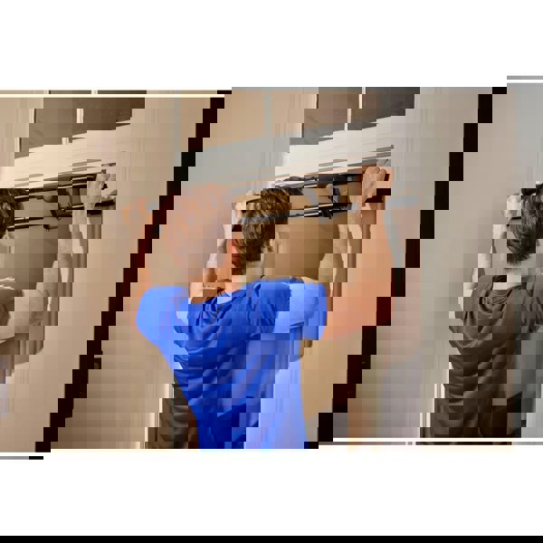 Person using a pull-up bar attached to a door frame in a home setting.