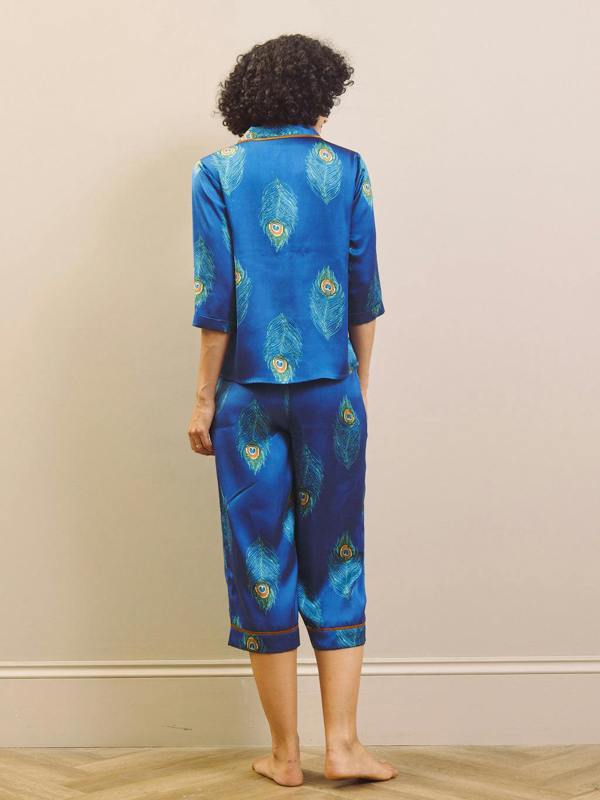 Person wearing a blue outfit with peacock feather patterns against a beige wall.