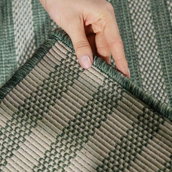 Hand touching a green and beige woven rug