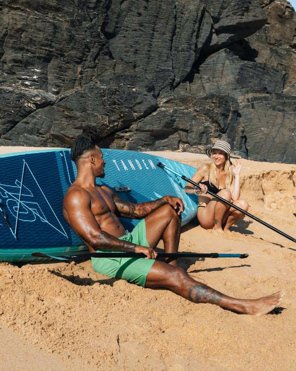 Couple enjoying time on the beach with a stand-up paddleboard and paddles.