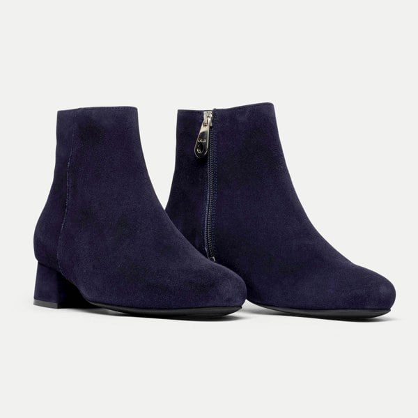 Pair of navy blue ankle boots with a zipper on a light gray background