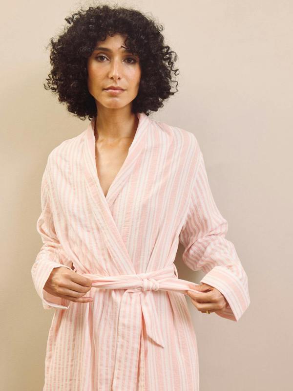 Woman wearing a pink striped robe against a plain background