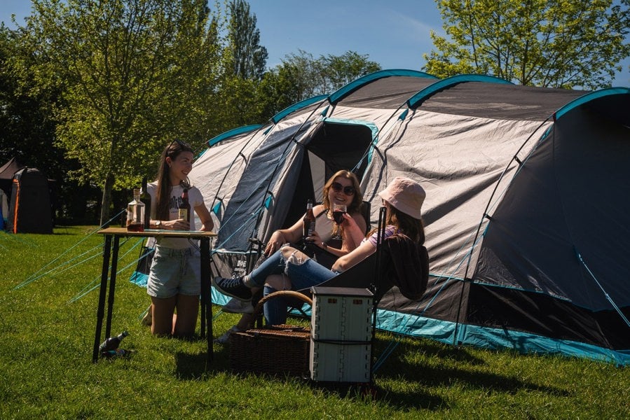 A group of young women enjoy a drink on a campsite outside the Stafford 6.0 OLPRO x Ed Stafford Tent