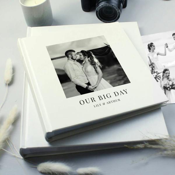 A personalised white square photo album featuring a black and white wedding photo and custom text on the cover, resting on a table.