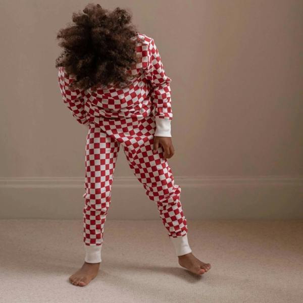 A child wearing a red and white checkerboard pattern organic cotton Christmas pyjama set with long cream turn-up cuffs.