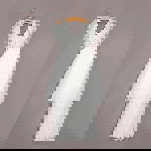 White dress with ruffled straps on a wooden hanger against a gray background