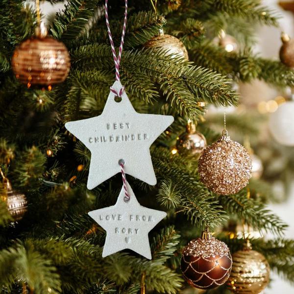 A handcrafted tiered white clay star decoration reading Best Childminder and Love From Rory, hanging on a Christmas tree surrounded by gold and bronze baubles.